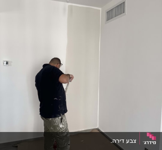 אדם צובע קיר בחדר עם מברשת צבע